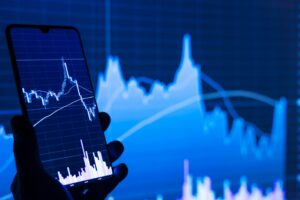 Smartphone displaying financial market chart against blue trading graphs